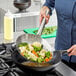 A person using an Emperor's Select stainless steel wok skimmer to cook vegetables in a wok.