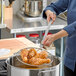 A person using a Choice round mesh skimmer to fry chicken in a pan.