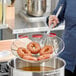 A woman using a Choice 14" Spiral Skimmer to hold a doughnut over a pot.