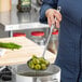 A woman using a Choice stainless steel skimmer to stir a pot of green beans.