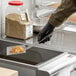 A person in black gloves using a Choice square fine mesh skimmer over a bowl of food.