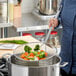 A person using a Choice 12" round mesh skimmer to cook vegetables in a pan.