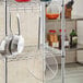 A metal rack with a Choice 12" Round Coarse Mesh Reinforced Skimmer hanging from it above a pair of pans.