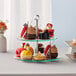 An Acopa 2-tier glass and stainless steel display stand with desserts on it on a table.