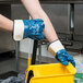 A person wearing Cordova Brawler smooth supported nitrile gloves holding a yellow bucket.