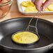 A person using an American Metalcraft chrome-plated egg ring to fry an egg in a pan.