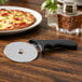 An American Metalcraft pizza cutter with a black handle on a table next to a pizza