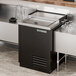 A black and silver refrigerated True glass froster on a metal counter.