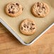 A Baker's Lane parchment paper sheet with three chocolate chip cookies on a tray.