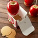 A wooden table with a Baker's Lane candy apple box filled with red candy apples with straws.