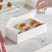 A hand putting a piece of chocolate into a white Baker's Lane candy box.