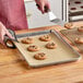 A hand using a spatula to put a cookie on a tray lined with Baker's Lane parchment paper.