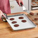A person cutting cookies on a Baker's Lane parchment paper lined baking sheet.