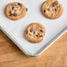 A Baker's Lane parchment paper lined sheet pan with four chocolate chip cookies.