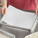 A person placing a Baker's Lane Quilon-coated parchment paper sheet on a baking tray.