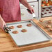 A person using a spatula to remove cookies from a Baker's Lane parchment paper-lined sheet pan.