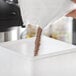 A person pouring brown powder into a white container.