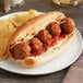 A meatball sub with cheese and tomato sauce on a plate.