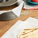 A tortilla on a white menu tissue on a table with a plate of food.