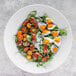 A salad with Crafty Counter Wunder Egg halves, tomatoes, and greens on a white plate.