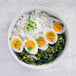 A white bowl of yellow food with eggs and rice.