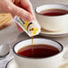 A hand pouring Honey 9 Gram Portion Packet into a cup of tea.