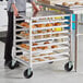 A woman standing next to a Regency undercounter sheet pan rack full of pastries.