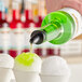 A person pouring Hawaiian Shaved Ice Margarita syrup into a cup of snow cone ice.