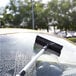 A windscreen scraper with a sponge and telescopic handle being used to clean a car windshield.