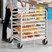 A woman using a Regency aluminum sheet pan rack to move bread.