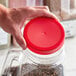 A person's hand holding a red 110/400 plastic lid on a jar.