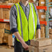 A man wearing a Lavex lime high visibility safety vest holding a stack of cardboard boxes.