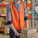 A man wearing an orange Lavex safety vest holding boxes.