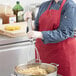 A woman in a red apron using a Fourt&#233; stainless steel round-faced potato masher to mix food in a pot.