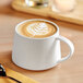 An Acopa Lore bright white porcelain cup filled with coffee with a leaf design in the foam.