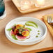 An Acopa Lore bright white porcelain plate with a slice of radish and a fork on a table.