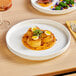An Acopa Lore bright white porcelain plate with a small dish of food on it.