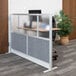 A Luxor modular wall room divider with frosted acrylic and gray panels dividing an office with a desk and plants.