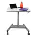 A Luxor light gray sit/stand student desk with a laptop, tablet, and notebook on it.