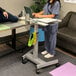 A woman in scrubs using a laptop on a Luxor adjustable-height student desk.