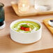 A white Acopa Lore porcelain bowl of soup on a table.