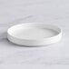 An Acopa Lore bright white porcelain plate with a raised rim on a marble surface.