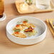 A white Acopa Lore porcelain deep plate with food on it on a table.