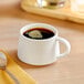 An Acopa Lore bright white porcelain espresso cup on a table with a spoon and a cup of coffee.