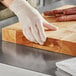 A person wearing gloves cutting sausage on a Choice wood cutting board.