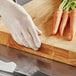 A person wearing white gloves cuts a carrot on a Choice wood cutting board.