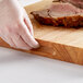 A person in gloves using a Choice wood cutting board to touch a piece of meat.