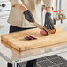 A person in gloves cutting meat on a Choice wood cutting board.