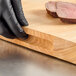 A person wearing black gloves cutting meat on a Choice wood cutting board.