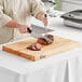 A person using a knife to cut meat on a Choice wooden cutting board.